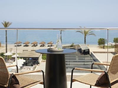 Balcon avec deux chaises et une table avec vue sur la mer et parasols sur la terrasse.