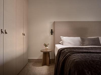 Chambre moderne avec lit gris, armoires blanches et table de chevet avec plante.