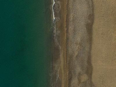 Vue aérienne d'une plage vide avec trois rangées de parasols au bord du rivage sablonneux.