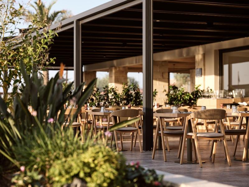 Restaurant extérieur couvert et chaleureux avec tables et chaises en bois dans un cadre naturel.