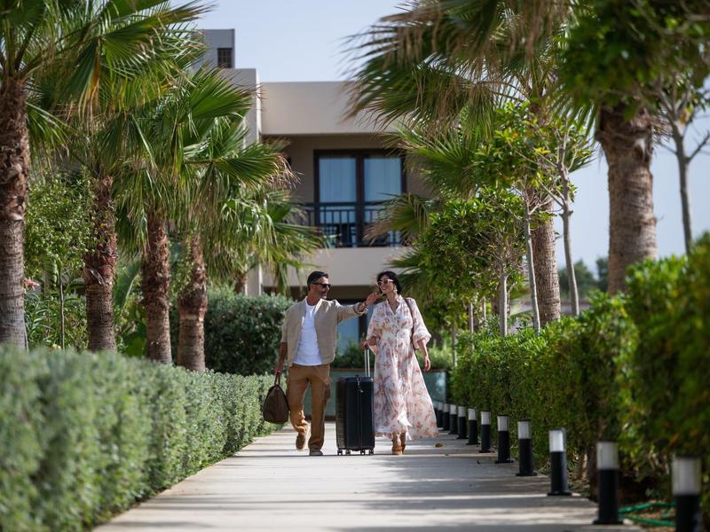 Couple avec bagages marchant le long d'un chemin bordé de palmiers vers un hôtel.