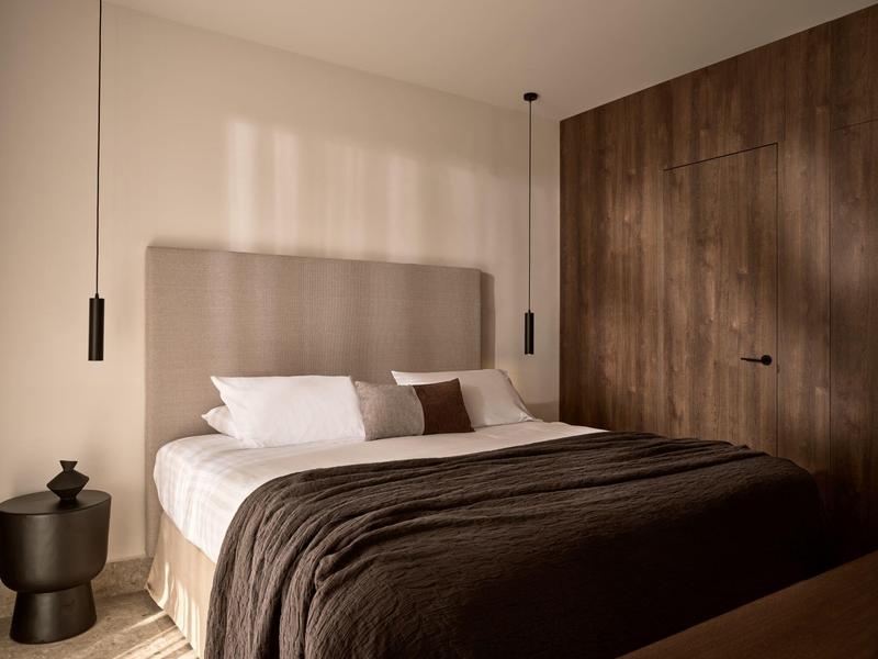 Chambre moderne avec grand lit, couverture marron foncé et mur en bois.