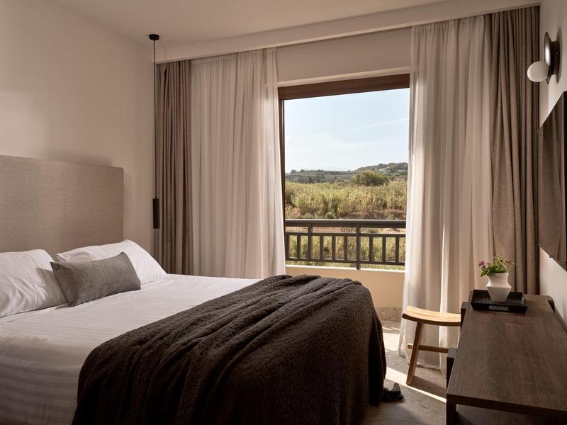 Chambre d'hôtel moderne avec grand lit et vue sur un paysage verdoyant.