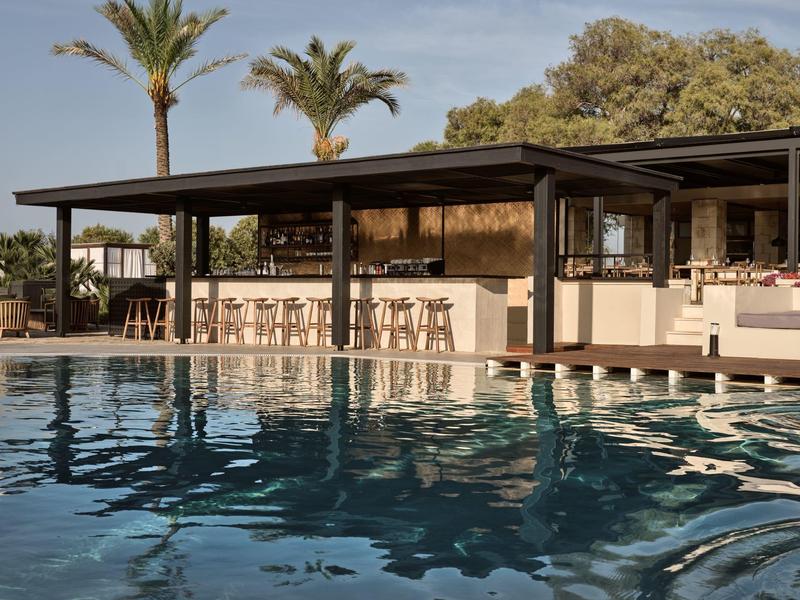Zone de piscine moderne avec bar et palmiers en arrière-plan.