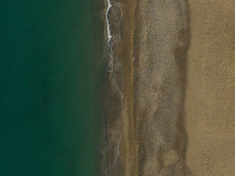 Vue aérienne d'une plage vide avec trois rangées de parasols au bord du rivage sablonneux.
