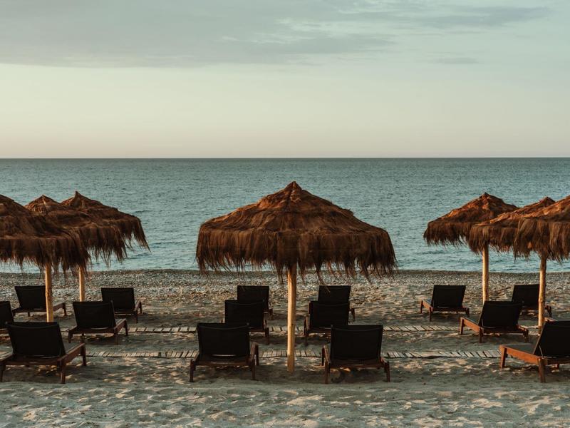 Rangée de chaises longues et parasols en paille sur une plage face à la mer.