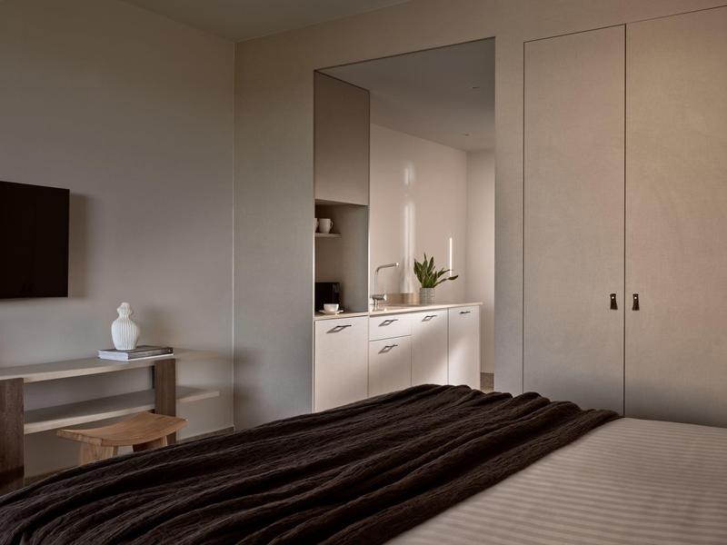 Chambre avec lit double, télévision et vue sur une cuisine avec des armoires blanches.