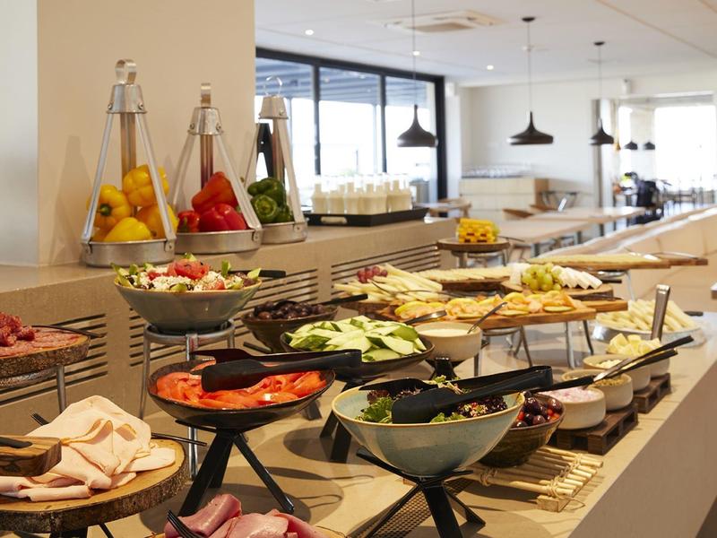 Buffet avec fruits frais, légumes, charcuterie et pâtisseries dans une salle à manger lumineuse.