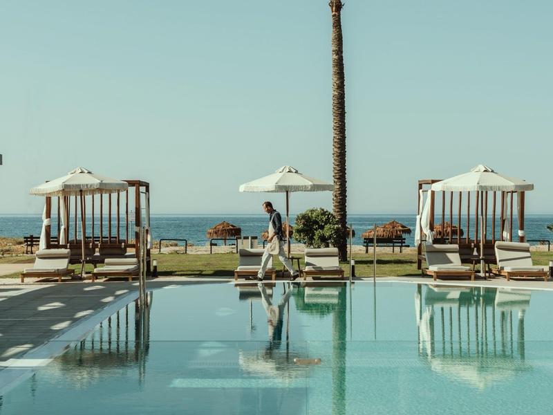 Piscine avec parasols, chaises longues et vue sur la mer sous un ciel clair.