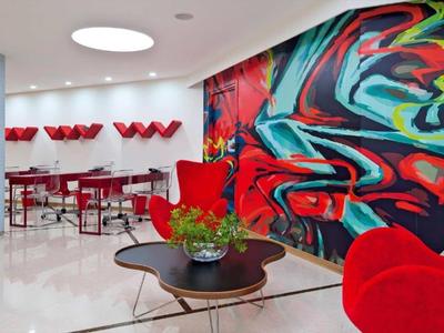 Modern hotel lobby with vibrant mural and red chairs.