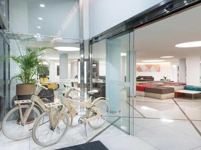 Bright modern hotel lobby with glass walls, white bicycles, and seating areas.