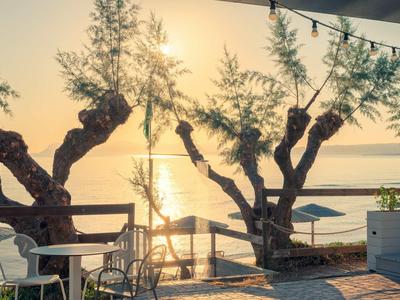 Sonnenaufgang über ruhigem Wasser mit Bäumen und einem Balkon mit Stühlen.