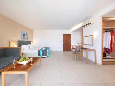 Bright hotel room with seating area, king-size bed, and desk with mirror.