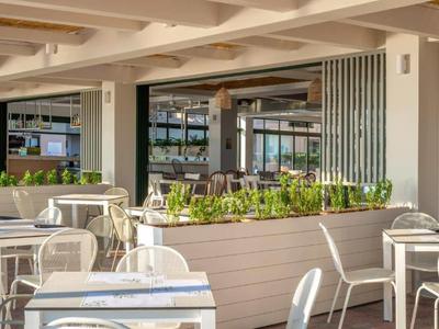 Bright hotel terrace with white tables, chairs, and plants, featuring a modern design.