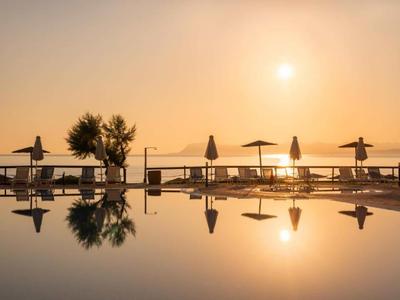 Poolbereich mit Liegestühlen und Sonnenschirmen bei Sonnenuntergang am Meer.