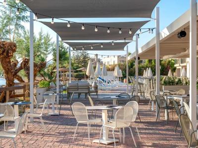Hotel outdoor area with chairs, tables, sun sails, and string lights.