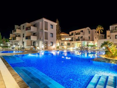Beleuchteter Hotelpool bei Nacht mit modernen Gebäuden im Hintergrund.