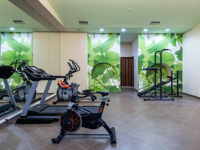 Moderner Fitnessraum mit Cardio-Geräten und großen grünen Pflanzenbildern an den Wänden.