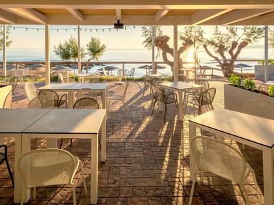 Sonnige Terrasse eines Cafés mit Tischen und Stühlen mit Blick auf den Strand und das Meer.