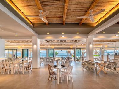 Großer Restaurantbereich mit Holztischen und Stühlen, Blick auf das Meer durch große Fenster.