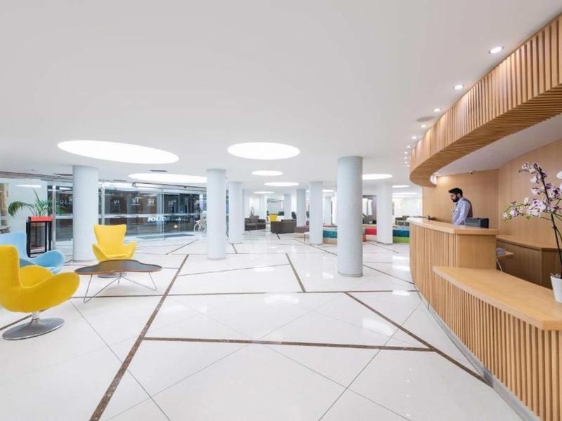 Bright, modern hotel lobby with yellow armchairs and wooden reception desk.