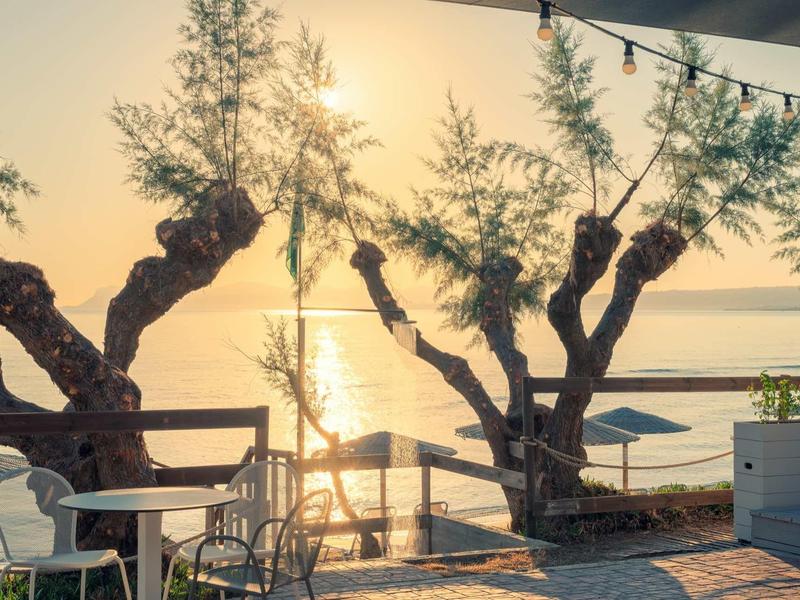 Sunrise over calm water with trees and a balcony with chairs.