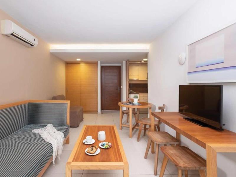 Modern hotel room with sofa, TV, dining table, and stylish lighting.