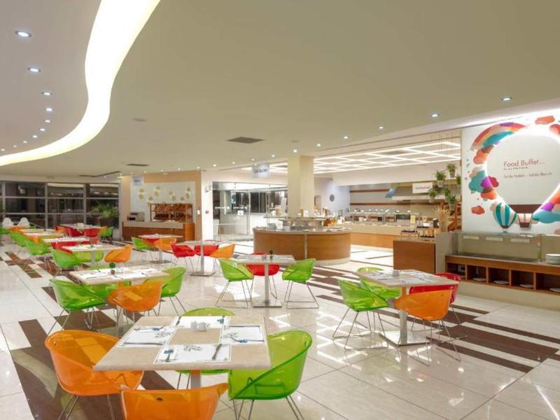Modern and bright hotel restaurant dining area with colorful chairs and buffet section.