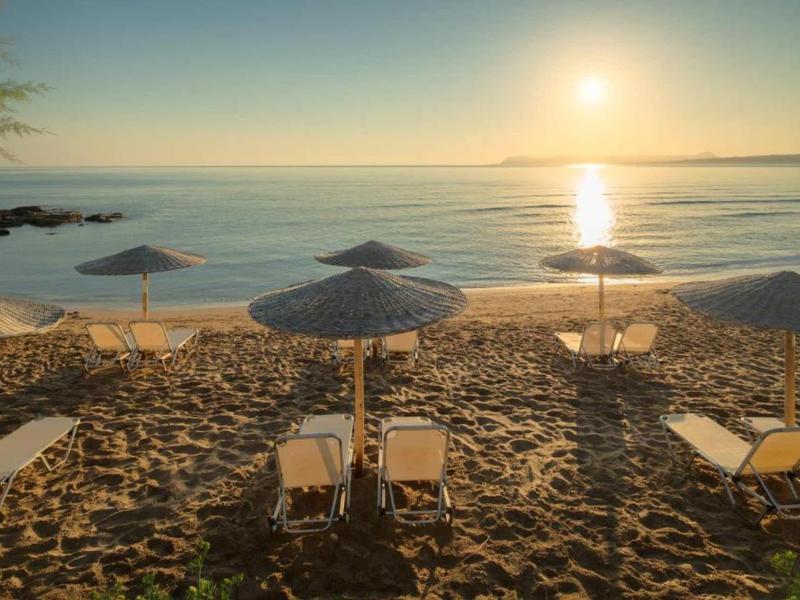 Beach with lounge chairs and umbrellas at sunset by calm sea