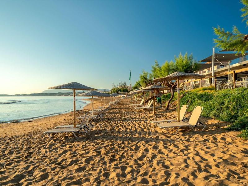Empty sandy beach with lounge chairs and umbrellas under clear sky.