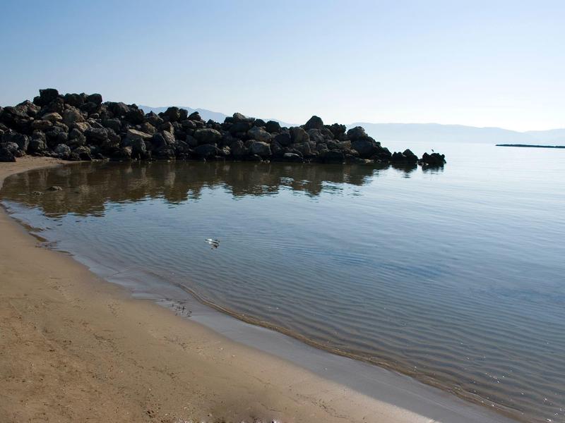 Helder water en zandstrand met rotsen langs de kust onder een heldere lucht