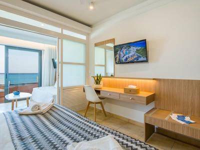 Moderní hotelový pokoj s postelí, pracovním stolem, TV a balkonem s výhledem na moře.