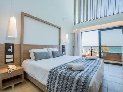 Moderní hotelový pokoj s manželskou postelí, nočními stolky a balkonem s výhledem na moře.