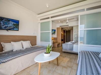 Moderní hotelový pokoj s oddělenými postelemi, konferenčním stolkem s rostlinou a televizí na stěně.