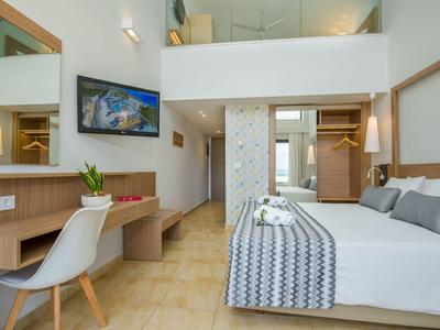 Světle a prostorně zařízený hotelový pokoj s manželskou postelí, psacím stolem, televizí a výhledem na balkon.