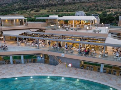 Moderner mehrstöckiger Hotelkomplex mit beleuchtetem Pool und Panoramablick auf hügelige Landschaft bei Dämmerung.