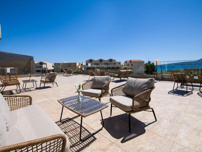 Moderner Außenbereich mit Sesseln und Tischen auf sonniger Terrasse mit Meerblick.