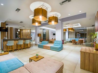 Modern eingerichtete Hotellobby mit Sitzbereichen, Bar und dekorativen Lampen an der Decke.