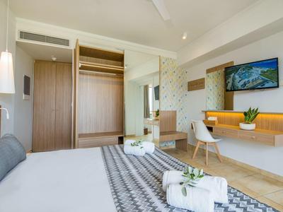 Chambre d'hôtel moderne avec grand lit, armoire ouverte et bureau avec télévision.