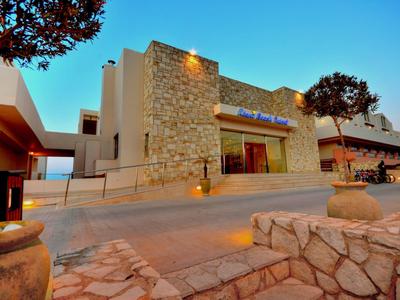 Kamenný vstup do hotelu při západu slunce, obklopený stromy a kamennými chodníky.