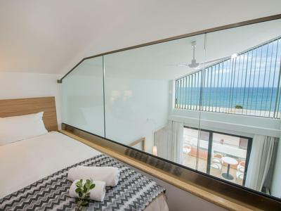 Nowoczesny pokój hotelowy z widokiem na morze przez duże okno, białą pościelą i dekoracyjnymi detalami.
