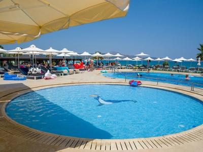 Kruhový bazén s lehátky a slunečníky s výhledem na moře za jasného dne.