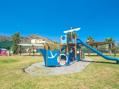 Barevné hřiště s lezecími konstrukcemi a skluzavkou na zelené trávě pod jasnou modrou oblohou.