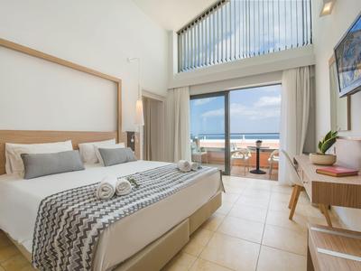 Helles Hotelzimmer mit Doppelbett, Schreibtisch und Balkon mit Meerblick.