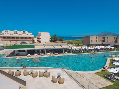 Großer Außenpool mit Liegestühlen und Sonnenschirmen vor Hotelgebäuden bei klarem Himmel