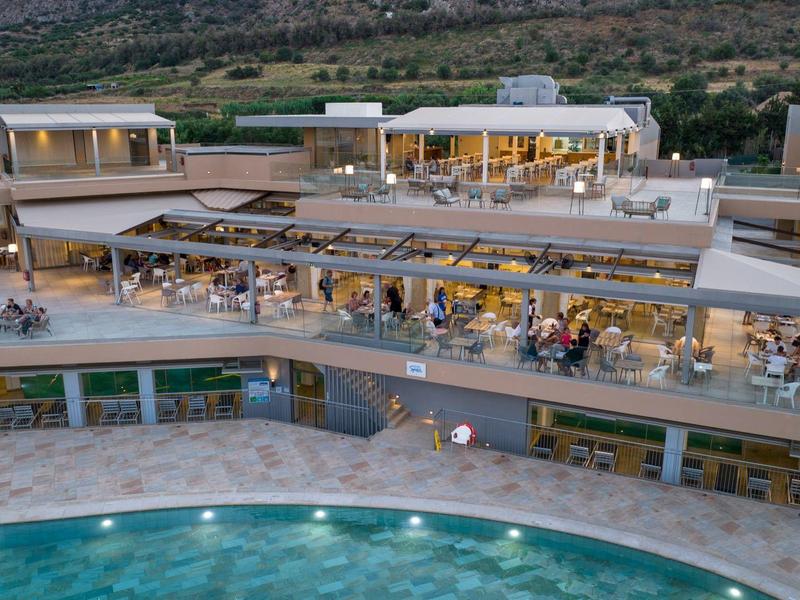 Luxusní resort s několika terasami a velkým bazénem za soumraku obklopený kopci.