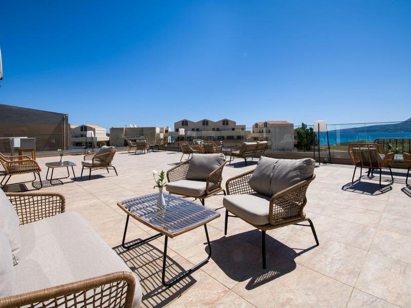 Venkovní terasa s moderními židlemi a stoly pod jasnou modrou oblohou poblíž budov.