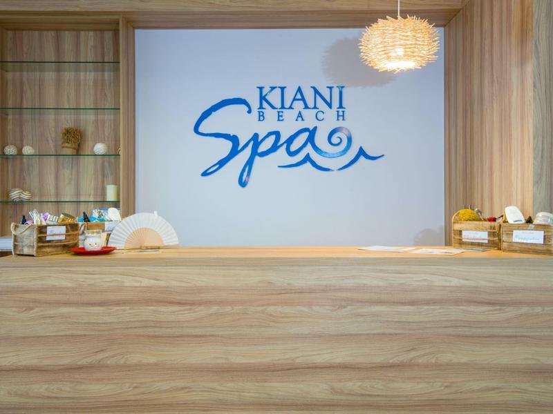 Dřevěná recepční přepážka s produkty spa a logem Kiani Beach Spa na stěně.