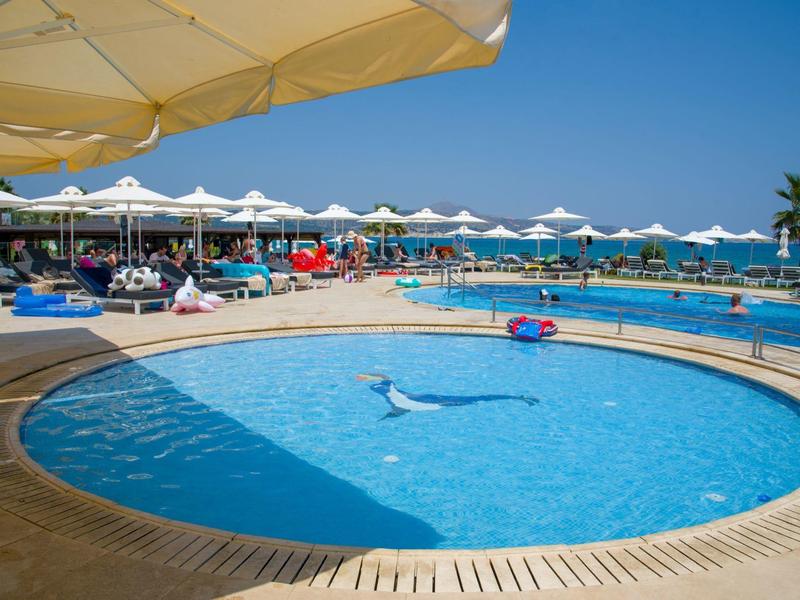 Kruhový bazén s lehátky a slunečníky s výhledem na moře za jasného dne.