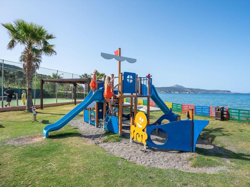 Dětské hřiště s pirátskou lodí u palmy u moře pod jasnou oblohou.